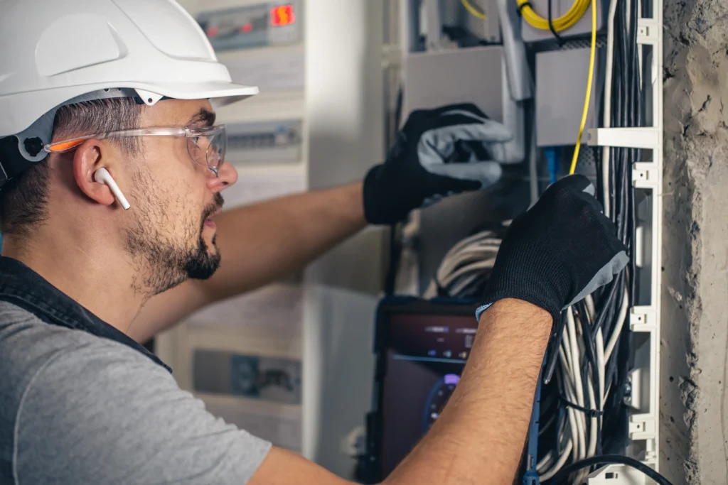 Elektryk firmy Konstelekt w kasku i okularach ochronnych wykonuje montaż rozdzielnicy elektrycznej